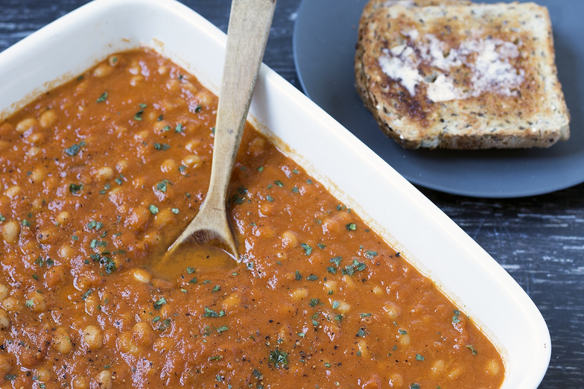 homemade baked beans in roasting dish with toast on plate in background