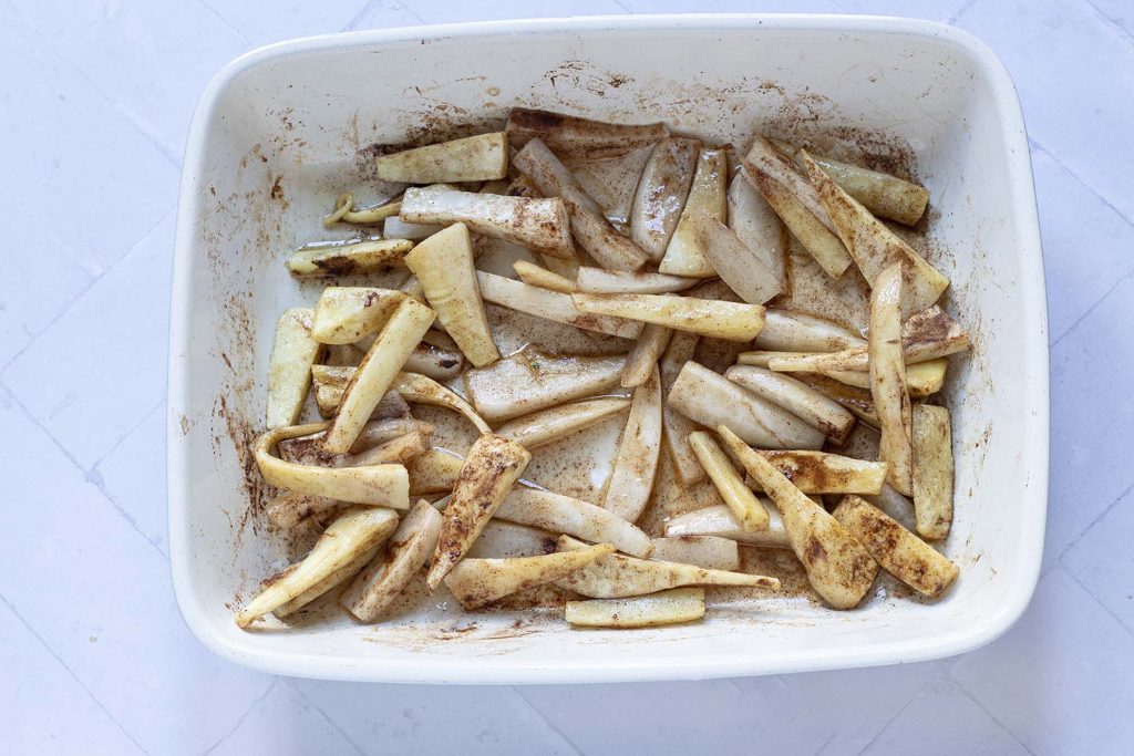 semi-cooked parsnips and turnip chips in roasting tin with cinnamon and maple syrup