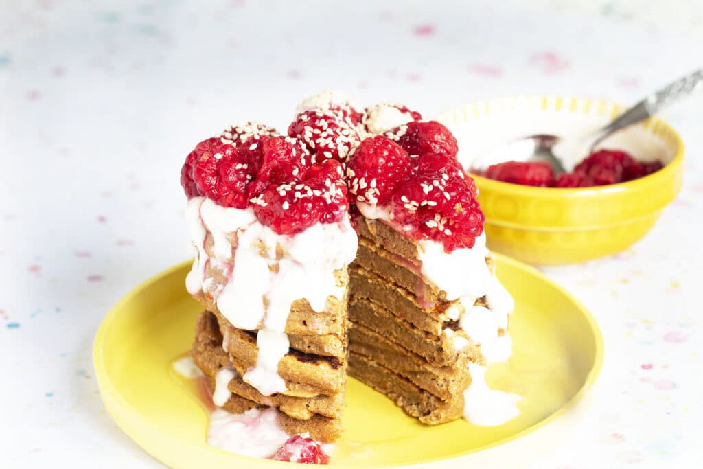 stack of sweet potato pancakes on yellow plate with yoghurt and raspberries