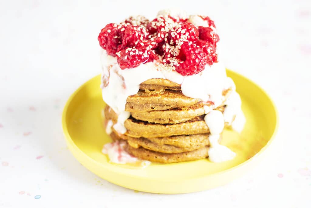 stack of sweet potato pancakes on yellow plate with yoghurt and raspberries