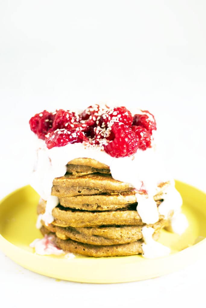stack of sweet potato pancakes on yellow plate with yoghurt and raspberries