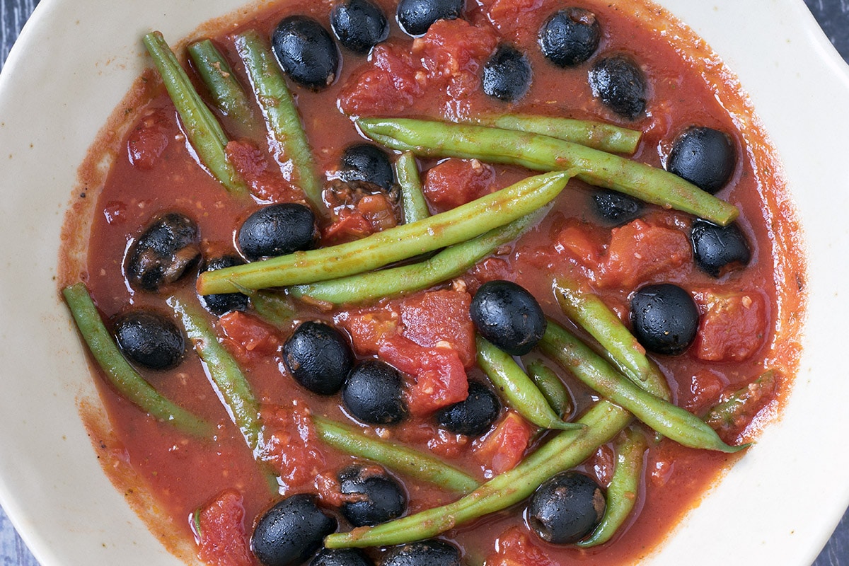 Green beans in tomato sauce with black olives close up shot