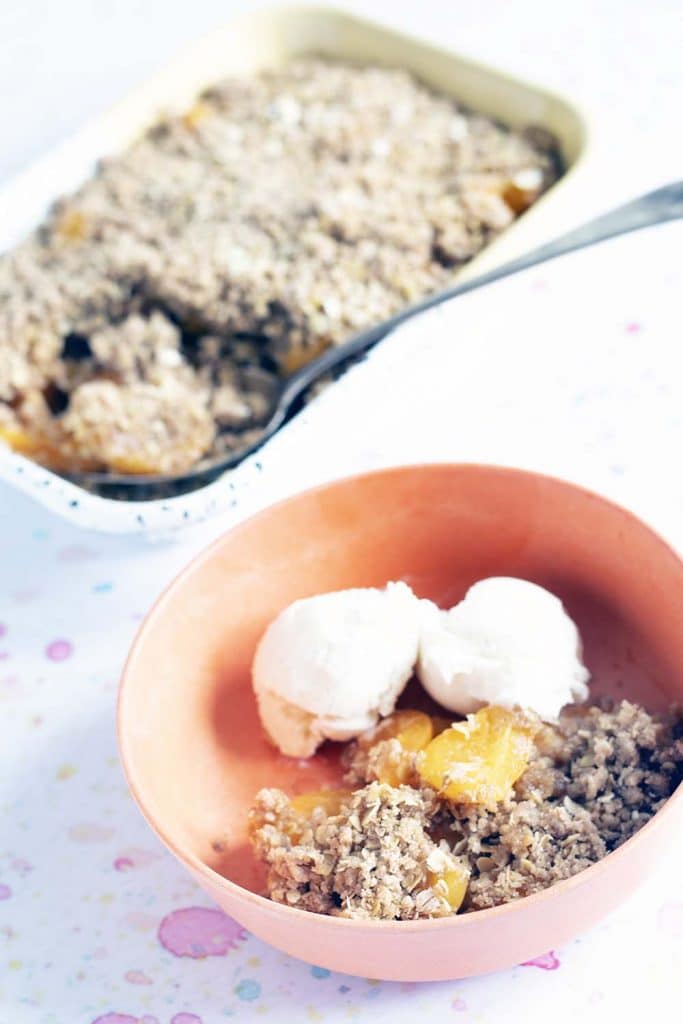 apricot crumble and ice cream in orange bowl with dish in background