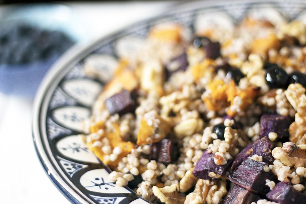 close up of Buckwheat salad in bowl with purple and orange sweet potatoes and blueberries