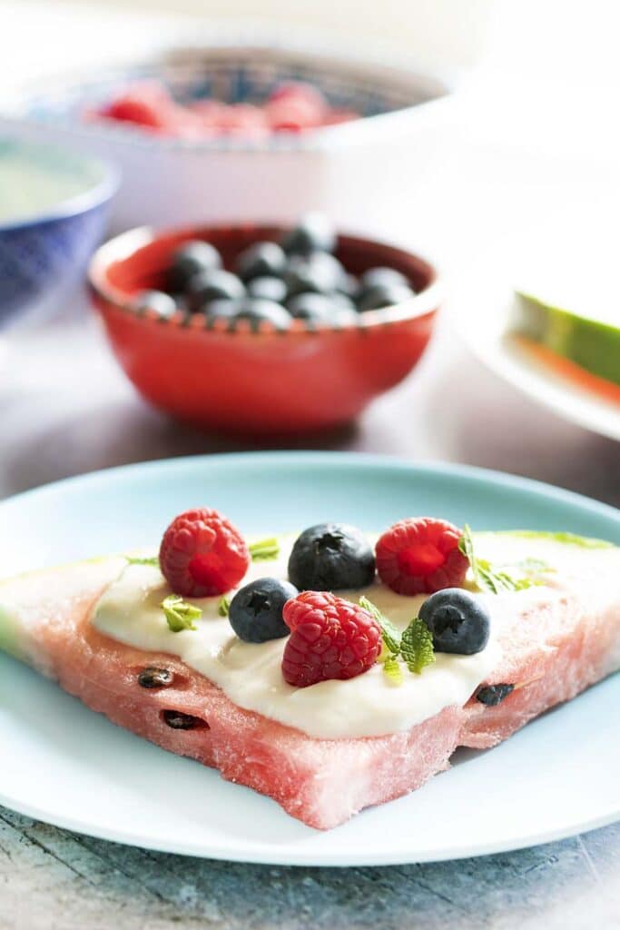 WATERMELON PIZZA ON BLUE PLATE WITH YOGHURT AND FRUIT