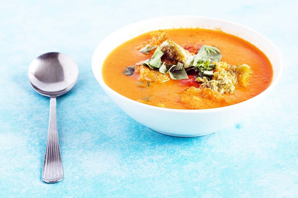 tomato pesto soup in white bowl on blue background