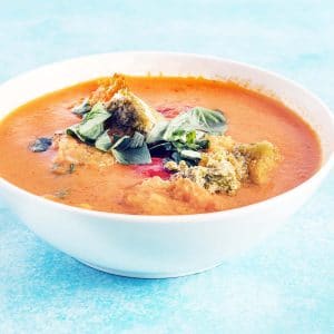 tomato pesto soup in white bowl on blue background