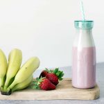 healthy strawberry milkshake in bottle with fresh bananas and strawberries on board