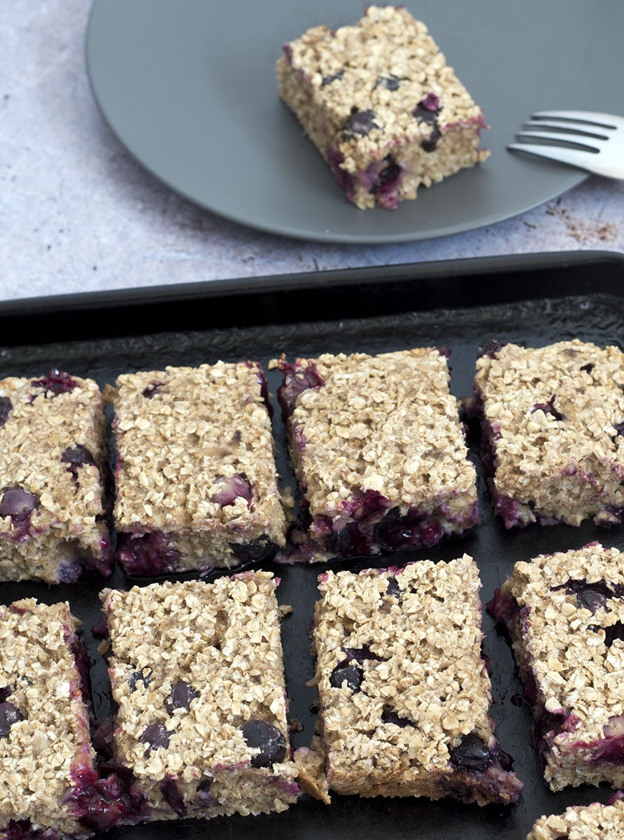 porridge bars with banana and blueberry on baking tray with single serving in background on a grey plate
