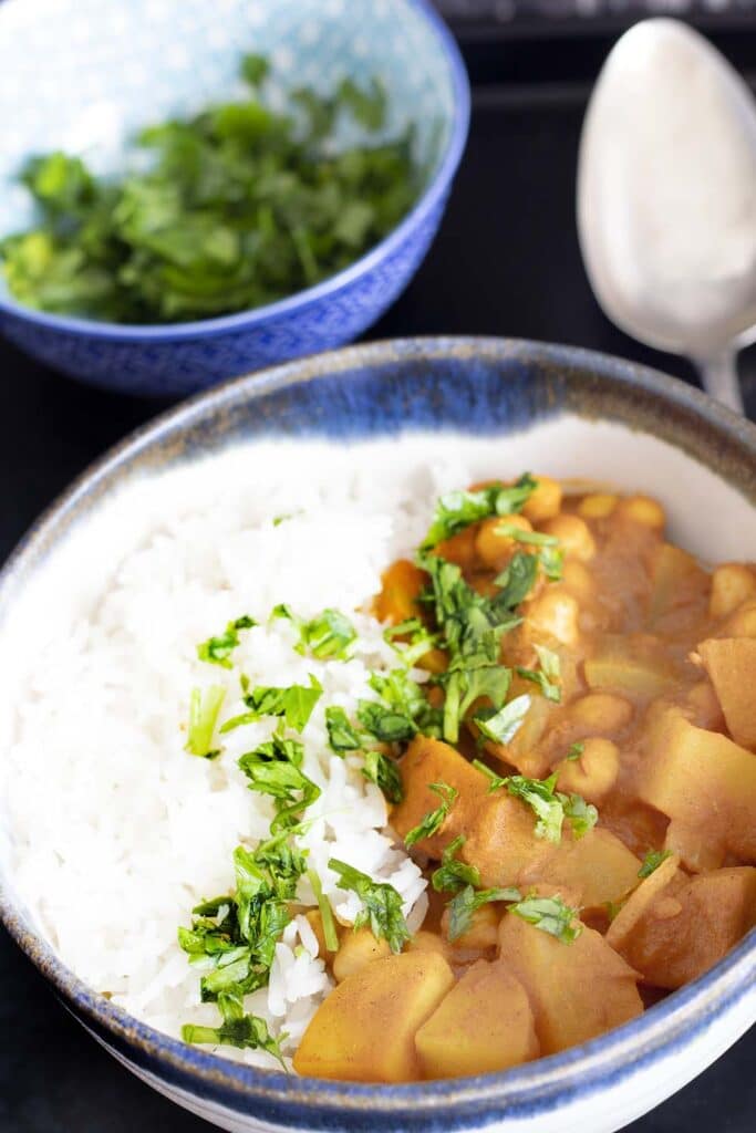 potato chickpea curry in bowl with rice and bowl of coriander in background