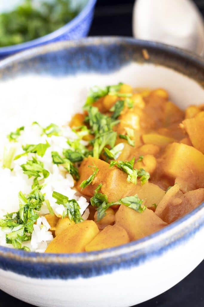 potato chickpea curry in bowl with rice and bowl of coriander in background