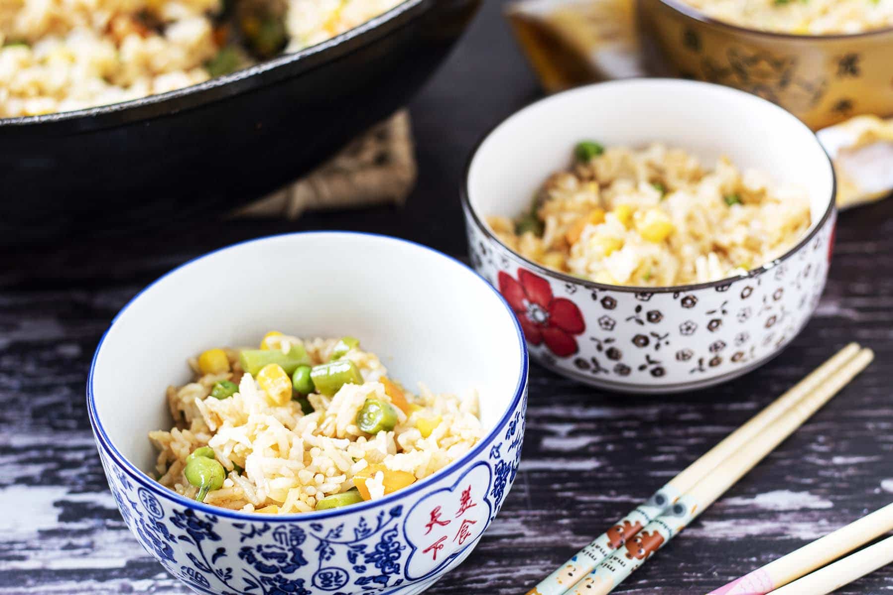 veggie fried rice in wok and bowls with chopsticks