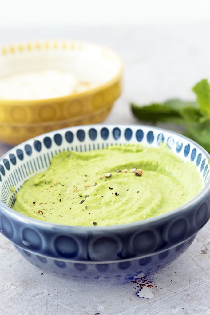 Pea and mint dip in blue bowl with mint sprigs and yellow bowl in background