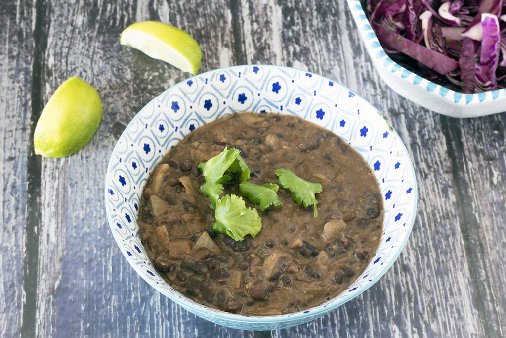 refried black beans in blue and white bowl with limes and cabbage salad