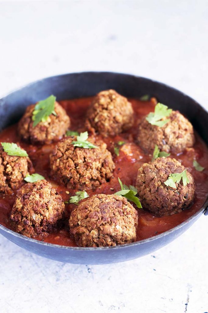 vegan meatballs in black dish with tomato sauce