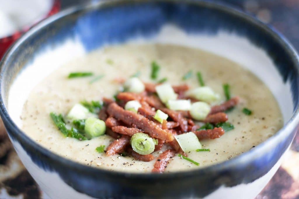 vegetarian baked potato soup with veggie bacon, spring onions and chives in blue and white bowl