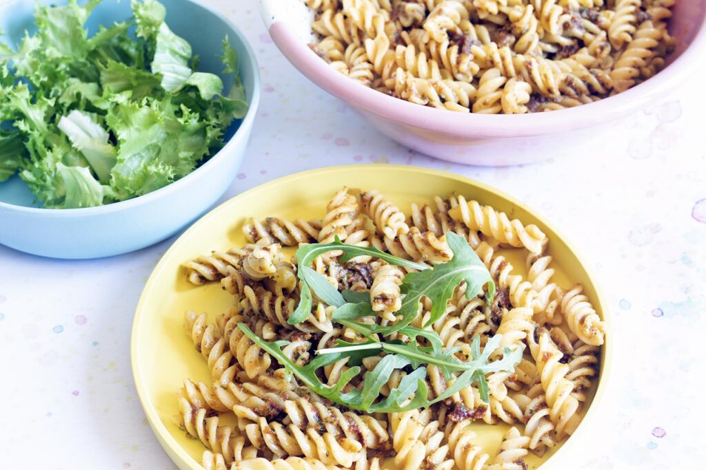 yellow plate with sundried tomato pasta pesto and rocket, bowl of lettuce in background