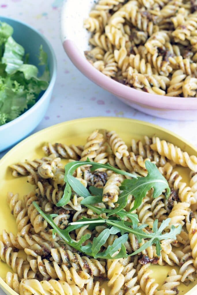 yellow plate with sundried tomato pasta pesto and rocket, bowl of lettuce in background