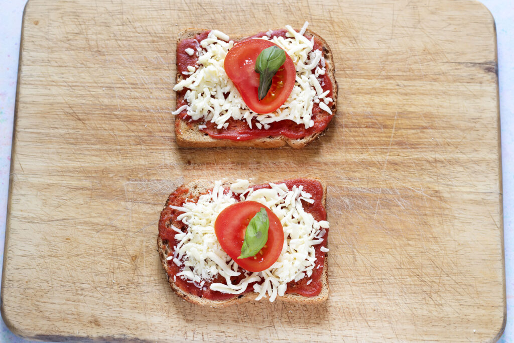 two slices of toast with tomato sauce, grated cheese, tomato and basil
