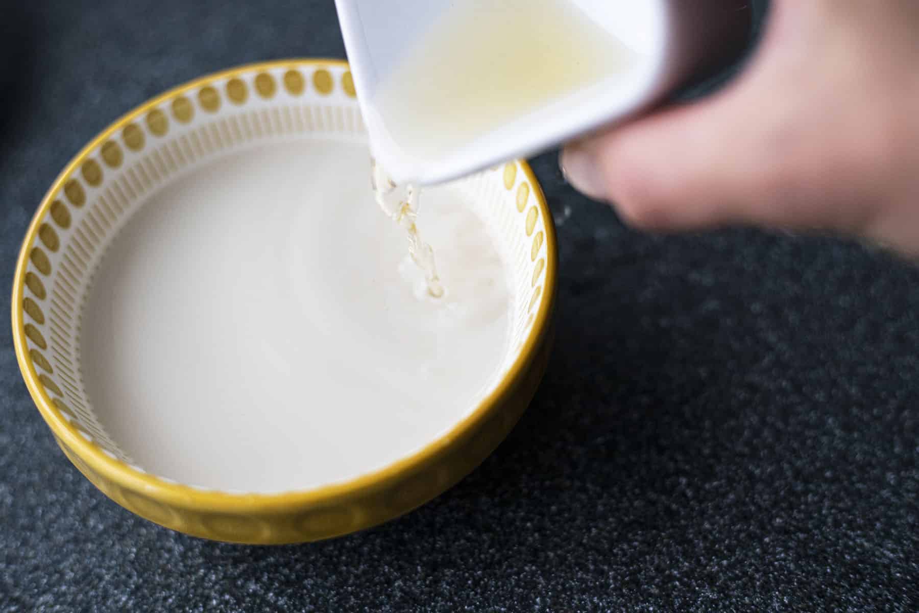 hand pouring cider vinegar into milk
