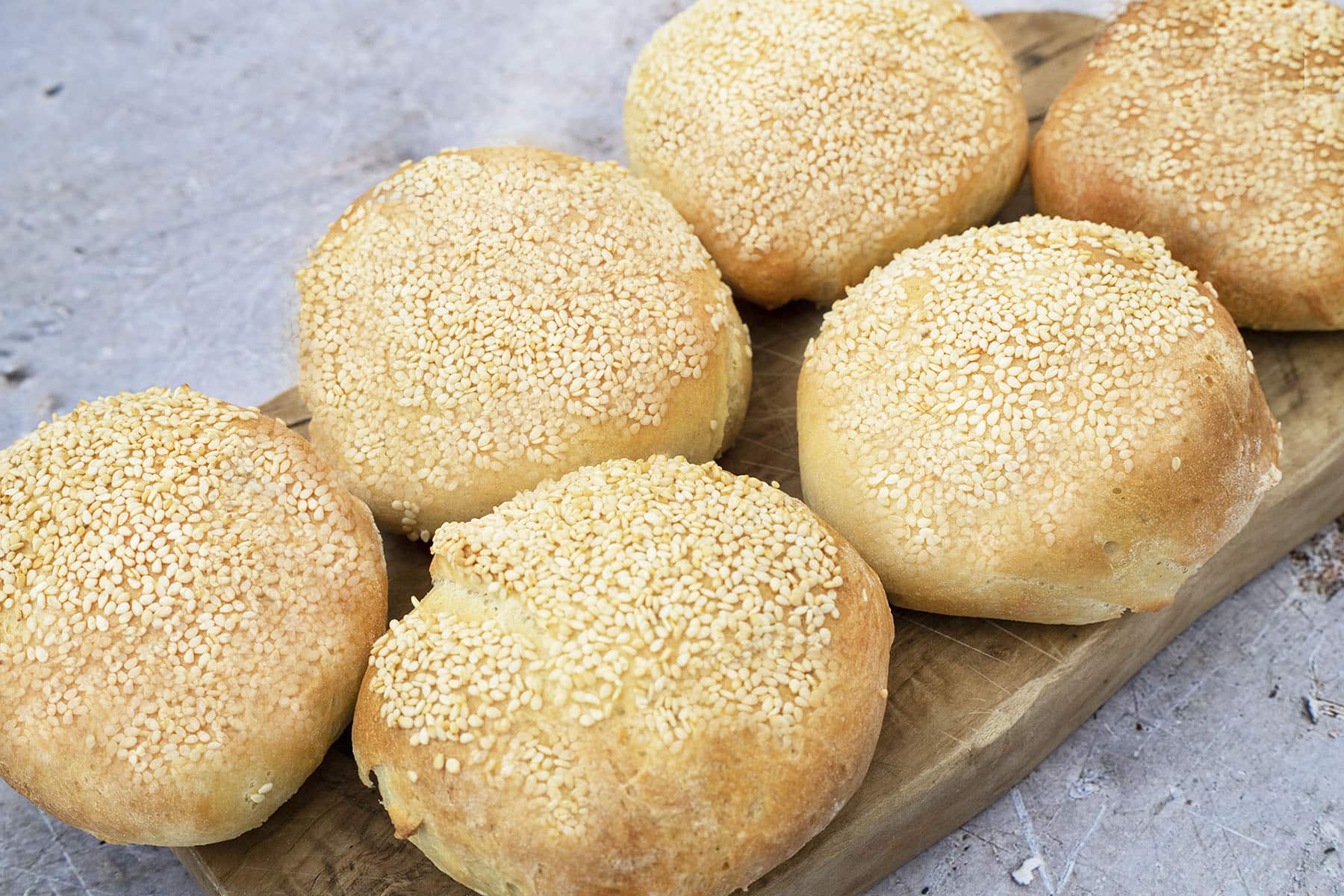white bread rolls covered in sesame seeds on board